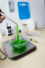 Naklejka premium The slime green substance in the laboratory dish is pulled with tweezers. Research and scientific discoveries on the table in the laboratory. High quality photo