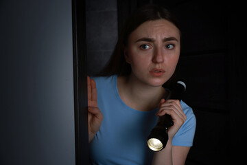 Fear of darkness. Scared young woman with flashlight indoors at night