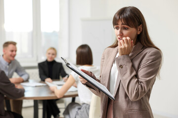 Glossophobia. Woman with clipboard feeling embarrassed during business meeting in office, selective focus