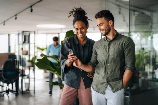 Diverse team of two business people working talking using smart phone walking in corporate office