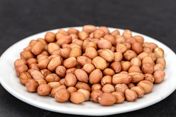 Obraz premium A lot of flesh raw peanuts on a white plate, ready to cook.