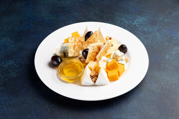 Assorted cheeses in a plate on a dark background.