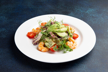 Salad with shrimps and avocado in a plate on a dark background.