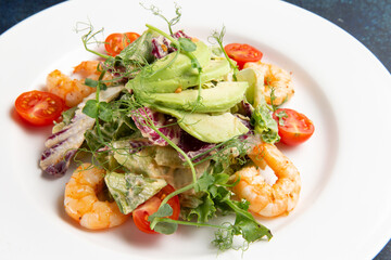 Salad with shrimps and avocado in a plate on a dark background.