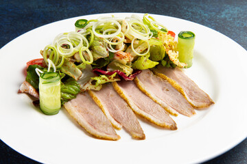 Salad and roast duck in a plate on a dark background.