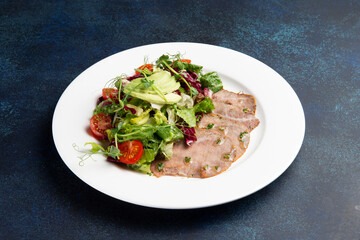 Beef tongue and salad in a plate on a dark background.