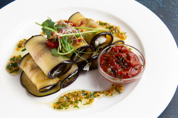 Eggplant rolls with cheese in a plate on a dark background.