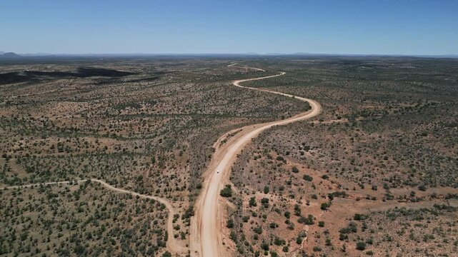Winding dirt road stretching through Namibia arid landscape between Windhoek and Sesriem as SUV navigates the path, panoramic aerial overview