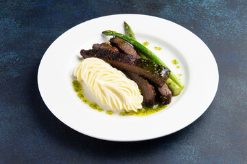 Steak with asparagus and mashed potatoes in a plate on a dark background.