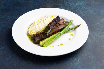 Steak with asparagus and mashed potatoes in a plate on a dark background.