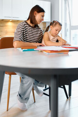 Fototapeta premium Mother helps daughter with homework at a modern dining table at home