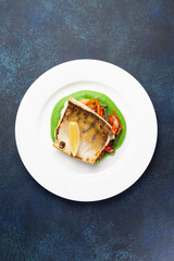 Cod steak on a bed of vegetables in a plate on a dark background.