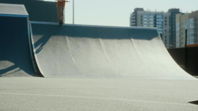 Side view low section shot of BMX rider riding bike through skate park, lifting front wheel and balancing on rear wheel while performing manual trick