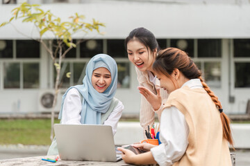Diverse female students excitedly collaborating around a laptop outdoors.
