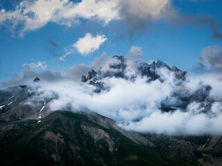 Montañas cubiertas de nubes bajo cielo azul en paisaje alpino