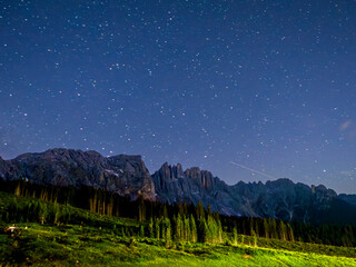 Paisaje nocturno alpino con cielo estrellado, bosque y montañas
