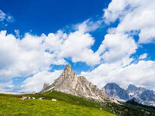 Montañas Dolomitas con pradera verde bajo cielo azul y nubes