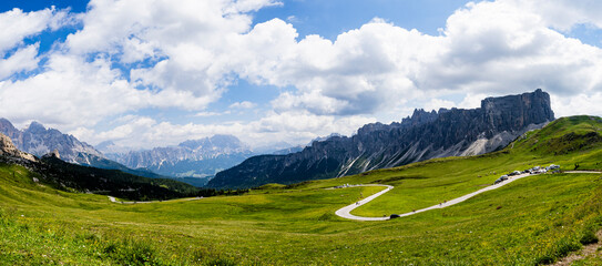 Carretera serpenteante en pradera alpina con montañas y cielo azul