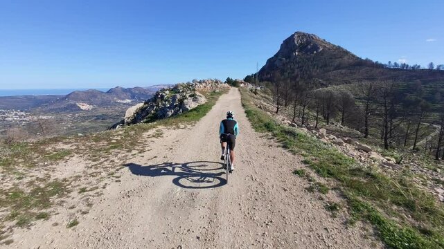 Cyclist rides gravel road, stunning mountain view.  Perfect for adventure, travel, and sports themes.  High-quality image for your projects.