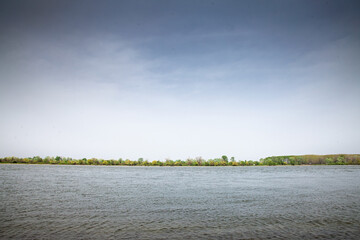 The Danube’s broad waters flow calmly through Serbia, framed by a gentle treeline on the distant...