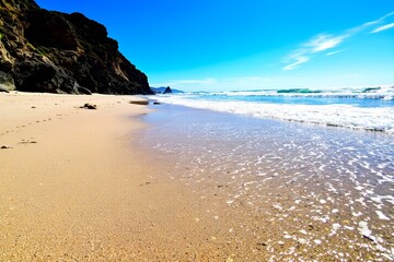 A pristine beach with crystal-clear waves gently lapping at the shore under a bright sun.