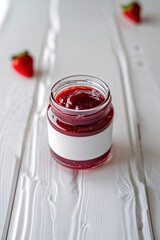 Delicious homemade strawberry jam in a glass jar on a white wooden table with fresh strawberries nearby