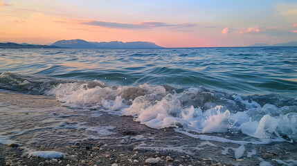 A scenic view of a beach at evening, with gentle sea waves, distant mountains, and a tranquil sunset sky.