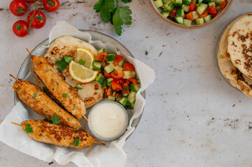 Chicken Kofta Kebab on wooden skewers with pita, garlic sauce Toum, parsley, lemon, cucumber and...