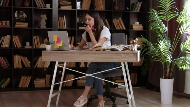 Beautiful student working on her school thesis on a laptop. Smart young woman sitting behind a desk studying an online course in an empty public library with modern design