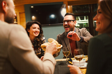 Cheerful friends sharing bread and wine laughing and having fun during a dinner at the restaurant