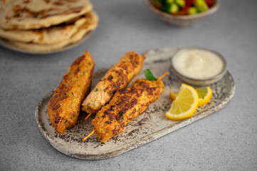 Chicken Kofta Kebab on wooden skewers with pita, garlic sauce Toum, parsley, lemon, cucumber and tomato. Shish kafta tavuk. Traditional Middle East food. Lebanese, Turkish cuisine. Food photography.