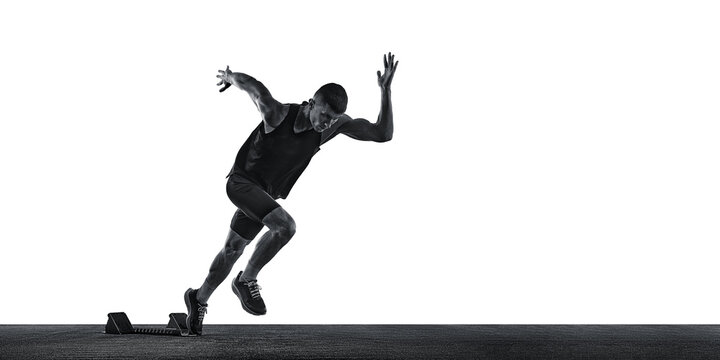 Dynamic photo of young athletic man, sprinter running from start line against white background. Monochrome photo. Concept of sport, healthy lifestyle, championship, action. Ad