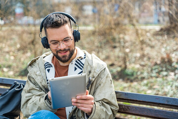 Young hipster businessman with cool attitude sitting in the park having video call on digital...