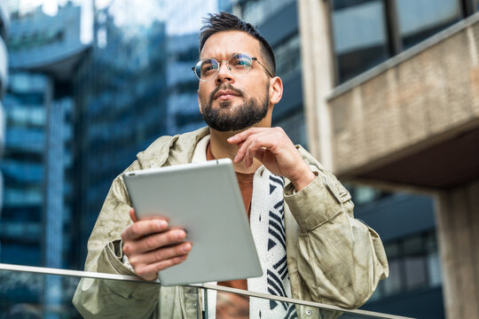 Young hipster businessman with cool attitude standing out of office building working digital tablet. Expatriate business person standing out of the crowd, intelligent design professional occupation.