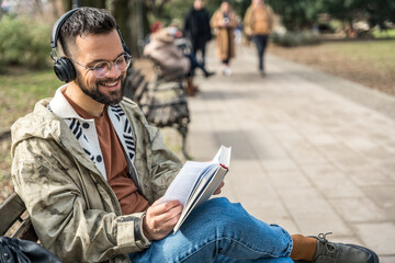 Young curious religious man, reading a book about religion, while sitting in the park on bench....