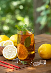 Glass of ice tea with lemon slices and mint outdoors on wooden table