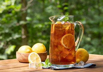 Pitcher of ice tea with lemon slices and mint outdoors on wooden table