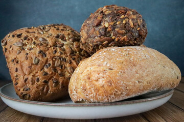 A variety of fresh artisanal bread rolls with seeds and grains on a rustic wooden table, set against a dark blue background