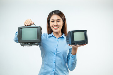 Smiling happy young Asian woman in blue shirt while holding two old TVs with blank screens isolated...