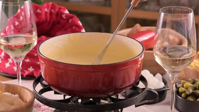 Cozy Swiss fondue setup with melted cheese, bread, pickles, and wine on a rustic table. advertising, social media campaigns, or food-related promotions. High quality 4k footage