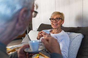 A cheerful senior couple enjoys a cozy morning with coffee, sharing smiles and conversation in a warm home setting, embracing love, connection, and relaxation