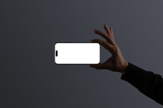 A hand holding smartphone in landscape orientation against a dark gray background. Isolated blank mockup surface to place your design. 