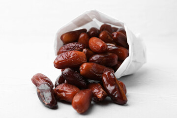 Tasty sweet dried dates in paper bag on white table, closeup