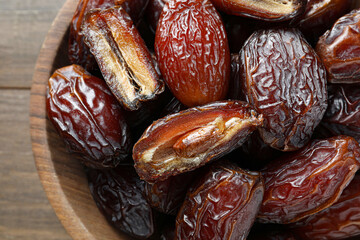 Many tasty dried dates in bowl on wooden table, top view