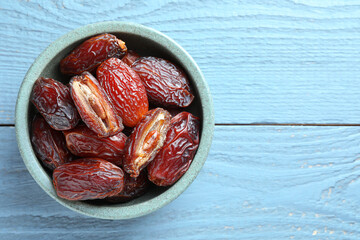 Many tasty dried dates in bowl on blue wooden table, top view. Space for text