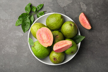 Fresh whole and cut guava fruits in bowl on grey textured table, top view