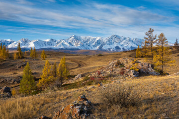 Fototapeta premium Mountainous landscape with snow-covered peaks and yellow trees under blue sky during autumn
