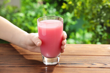 Woman with glass of guava juice at wooden table, closeup