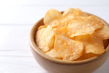 Tasty potato chips in bowl on white wooden table, closeup. Space for text