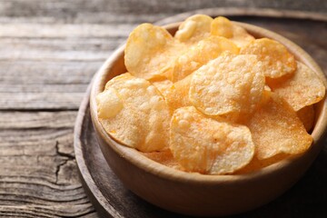 Tasty potato chips in bowl on wooden table, closeup